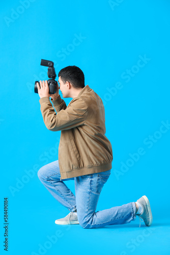 Young male photographer with professional camera on blue background