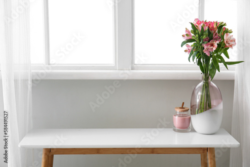 Vase with alstroemeria flowers and candle on table near window