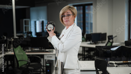 Caucasian business woman pointing on alarm clock in office. 