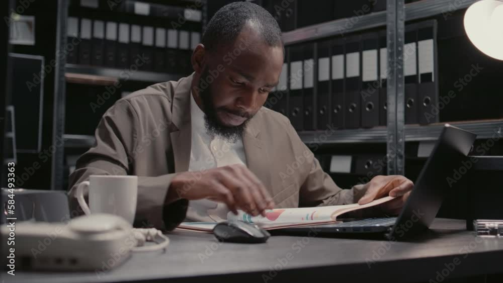 Male inspector reading witness statements and clues to find suspect, using case files and surveillance footage in police archive. Detective conducting criminal investigation. Handheld shot. Male inspector reading witness statements and clues to find suspect, using case files and surveillance footage in police archive. Detective conducting criminal investigation. Handheld shot.