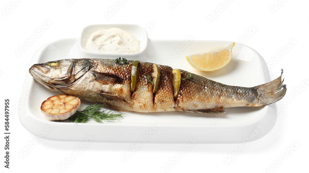 Plate with delicious baked sea bass fish, garlic, slice of lemon and sauce on white background Plate with delicious baked sea bass fish, garlic, slice of lemon and sauce on white background