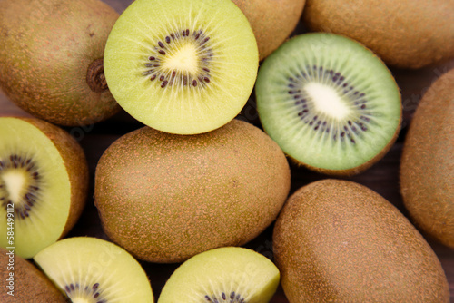 Many whole and cut fresh kiwis on wooden table, closeup