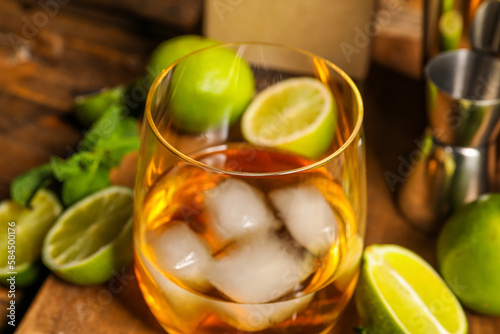 Glass of rum with ice, mint and lime on wooden table, closeup