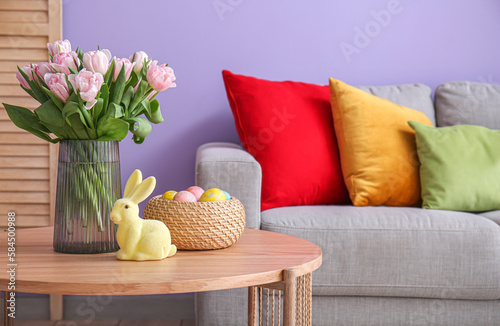 Vase with tulips, Easter rabbit and eggs on table in living room