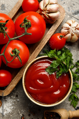 Bowl with tasty ketchup and fresh vegetables on grunge background