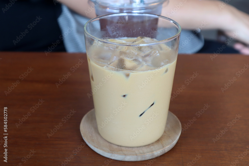 Glass of Thai style iced espresso with milk on wooden table in coffee shop. Thai iced coffee (gafae yen) is a beverage you can find on just about any street corner in Thailand. Glass of Thai style iced espresso with milk on wooden table in coffee shop. Thai iced coffee (gafae yen) is a beverage you can find on just about any street corner in Thailand.