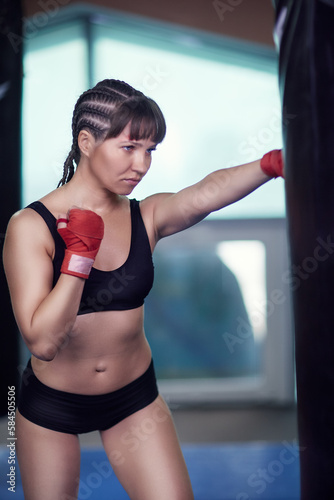 Female fighter with a boxing taping bandage on hands boxing on a punching bag . © Serg Zastavkin