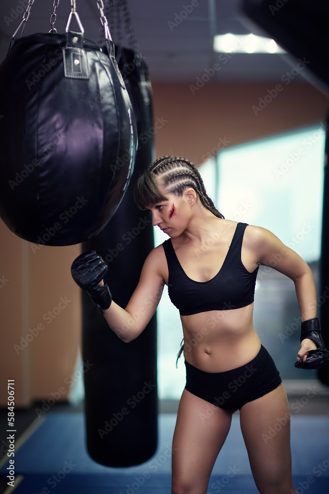 Female fighter with a boxing gloves on hands hboxing on a punching bag.