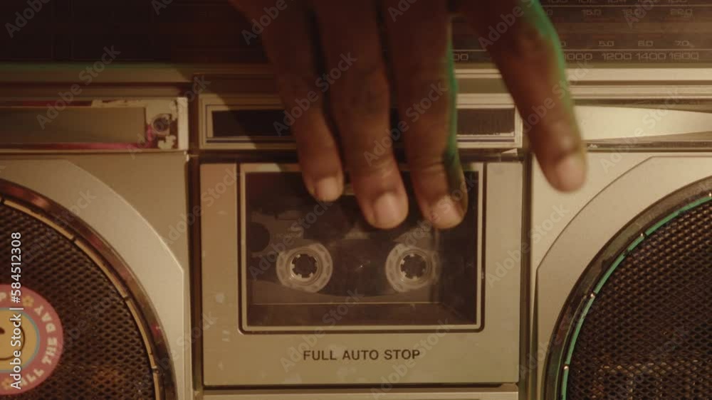 Man inserting compact audio cassette into retro ghetto blaster, pressing turn on button and playing the music. Warm soft light, close-up shot