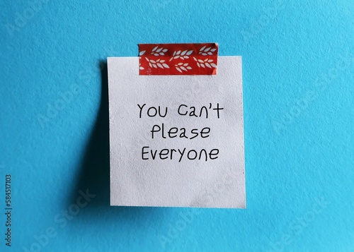 White note stick on blue background with handwritten text You Can’t Please Everyone - self reminder to stop trying to please everyone and be your authentic self