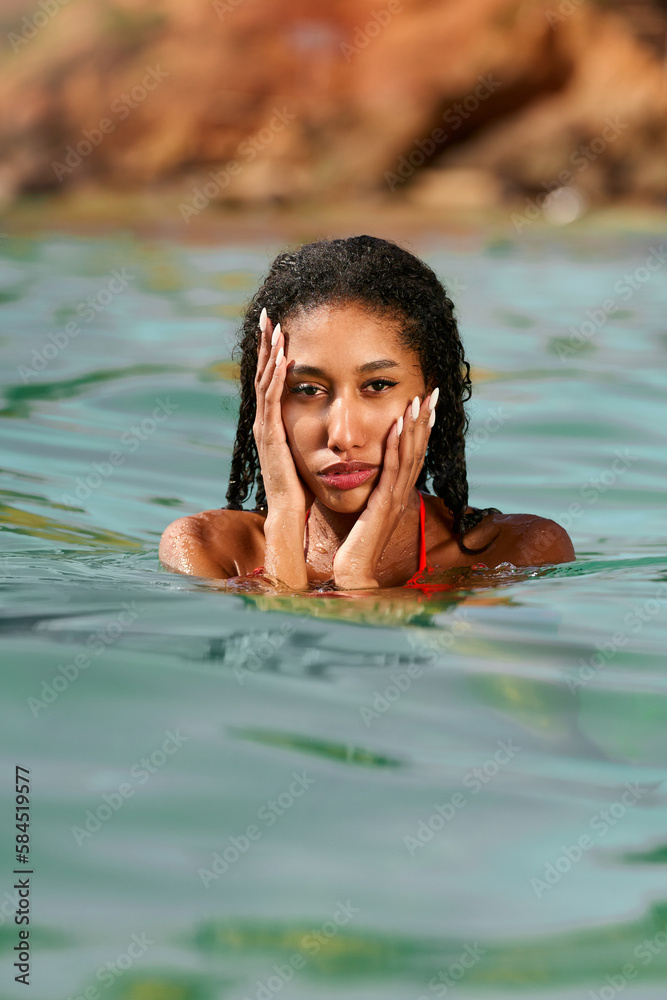 Portrait of serene looking attractive young black female posing in bikini in water. African model posing in the sea. Multiracial woman posing at the beach in ocean. Fashion portrait of black woman