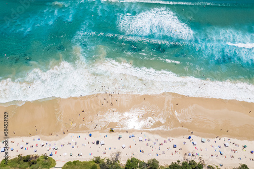 A busy beach day looking down at beach goers as the surf comes in.