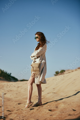 Wallpaper Mural a slender woman in a light long jacket, in black glasses, with a bag slung over her shoulder, stands on the sand against the blue sky Torontodigital.ca