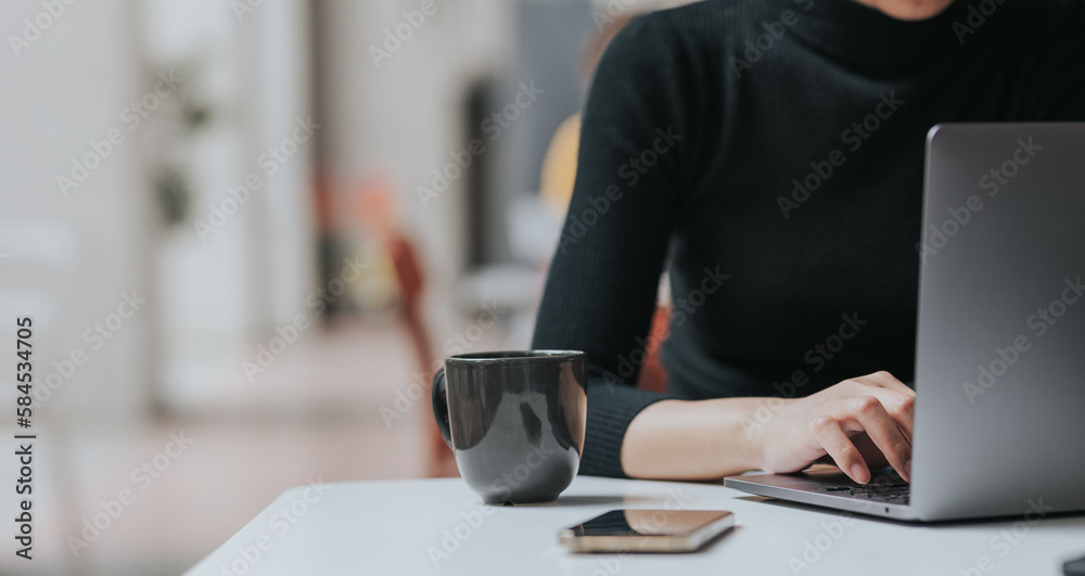 Young Asian woman using smartphone and laptop working remotely at coffee shop.