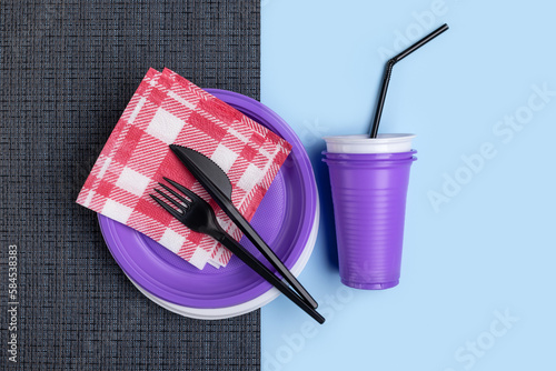 Plastic purple and white crockery, cutlery on a bicolor background. Studio shot, close-up.