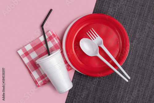 Plastic red and white crockery, cutlery on a two-tone background. Studio shot, close-up, top view.