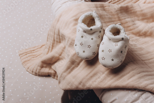 Soft baby shoes, booties on beige cocoon, baby nest for newborn over cribs in nursery. Childhood concept. Eco-friendly safe goods and toys for children. Light kid's room interior. Time for sleep photo