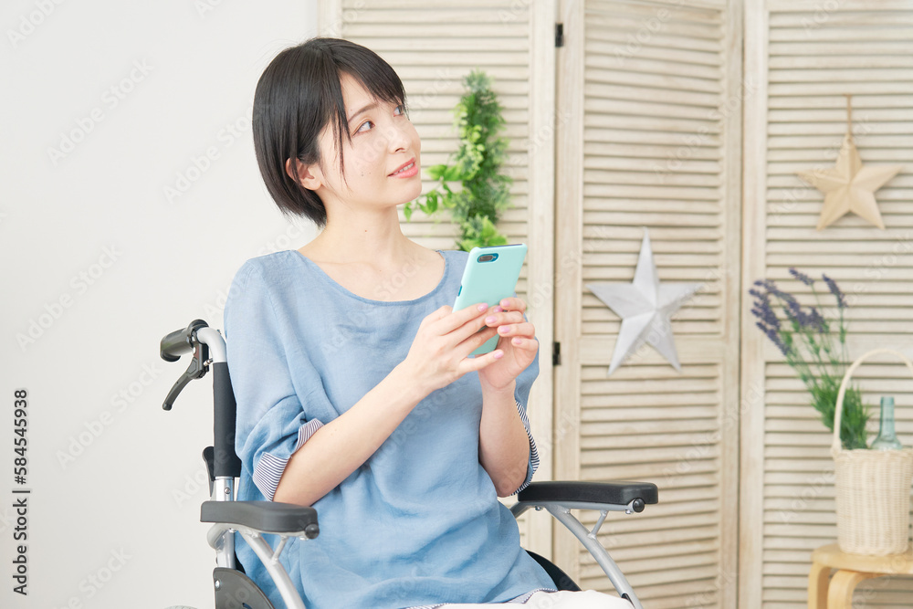 リビングでスマホを使う車椅子に乗った女性 リビングでスマホを使う車椅子に乗った女性