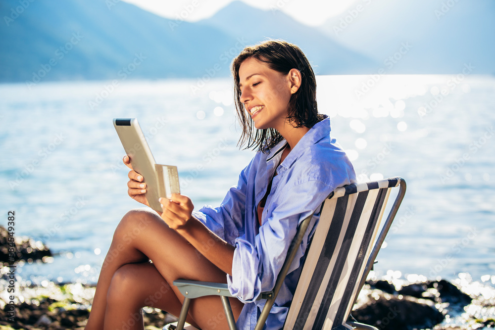Happy woman with digital tablet and credit card buying online sitting near the sea. Happy woman with digital tablet and credit card buying online sitting near the sea.