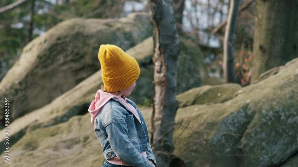 Portrait of smiling attractive little girl kid in knit yellow beanie sitting on big stones at calm spring forest. Beautiful happy cute kid enjoy outdoors, inhale fresh mountain air. Wanderlust concept Portrait of smiling attractive little girl kid in knit yellow beanie sitting on big stones at calm spring forest. Beautiful happy cute kid enjoy outdoors, inhale fresh mountain air. Wanderlust concept