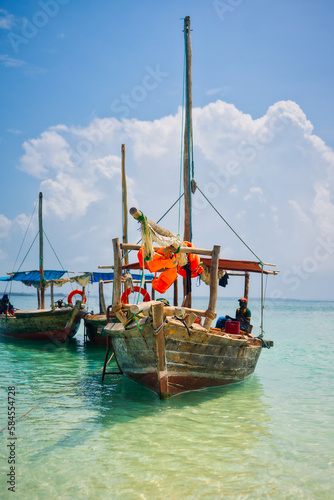 Fototapeta Naklejka Na Ścianę i Meble -  Experience the beauty of a traditional Zanzibar fishing boat as it rests in the clear waters near the beach of a tropical island, ideal for summer travel and fishing boats.