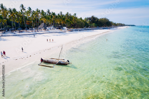 Take in the stunning scenery of Zanzibar's tropical coast from above, as fishing boats rest on the sandy beach at sunrise. The view from the top reveals clear blue waters, green palm trees, and even 