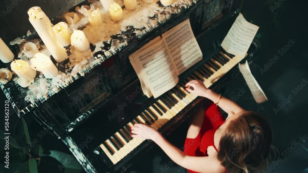 female musician hand touches white black key with passion fast. Woman plays the piano in evening red dress sexy back girl pianist creating music top view. dark room candles light paper pages falling