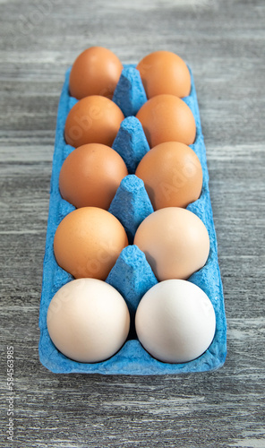 Close-up of a dozen fresh chicken eggs in a blue cardboard tray on a gray wooden textured background