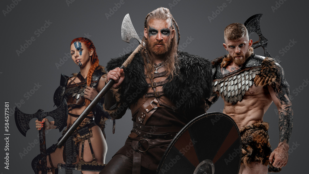 Studio shot of ancient vikings with fur and axes against gray background.