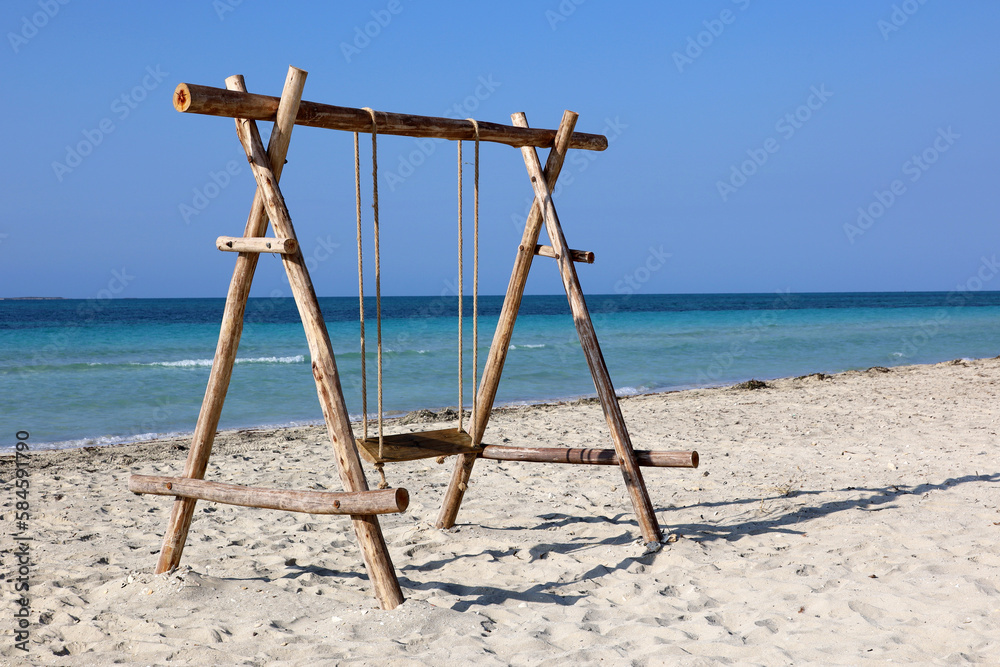 Wooden swing on a sand against the blue sea. Beach holidays on resort Wooden swing on a sand against the blue sea. Beach holidays on resort