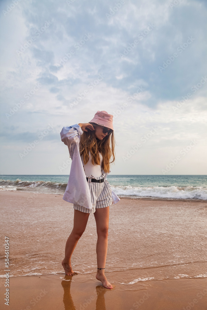 Full length young traveler woman in beachwear walking along sunny summer sandy beach. Relaxing and enjoyable vacation on tropical ocean. Travel vacation concept, summer holiday. Copy ad text space