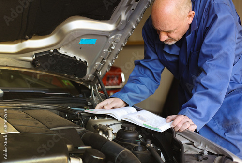 Mechanic man holding and reading the car user manual or user instruction to checking or fixing engine of modern car in garage. Car maintenance or service before driving concept. photo