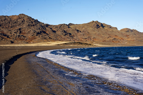 Plage de sable noir dont les eaux sont prises par la glace et la neige en Islande faisant face à une montagne puissante
