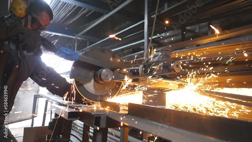 Industrial worker with circular saw sawing steel in workshop. Man in safety protection wear use saw cutting machine to cut metal. Craftsman grinding metal. Sparks fly from hot metal. Slow motion photo