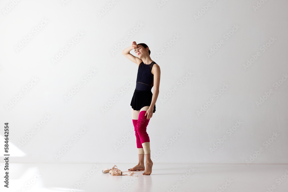 Exhausted beautiful ballerina standing and holding hand at head to rest with closed eyes over white background