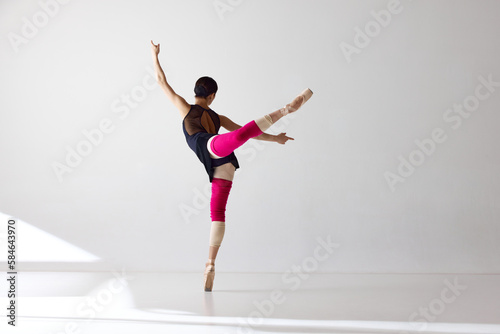 Back view. Ballet dancer standing wearing pointe shoes dancing on fingertips over white background