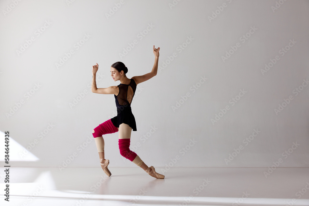One young ballerina wearing pointe shoes dancing on fingertips over white background