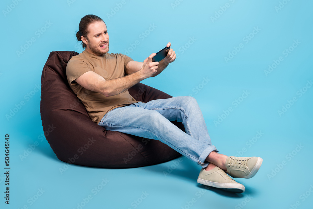 Full length photo of cheerful pretty man wear beige t-shirt bean bag watching video gadget emtpy space isolated blue color background - obrazy, fototapety, plakaty 