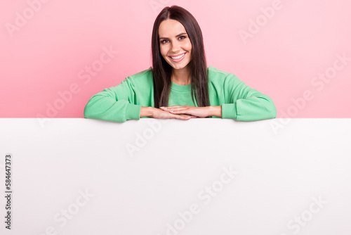 Portrait of optimistic satisfied pretty girl straight hairdo wear green pullover hold hands on placard isolated on pink color background