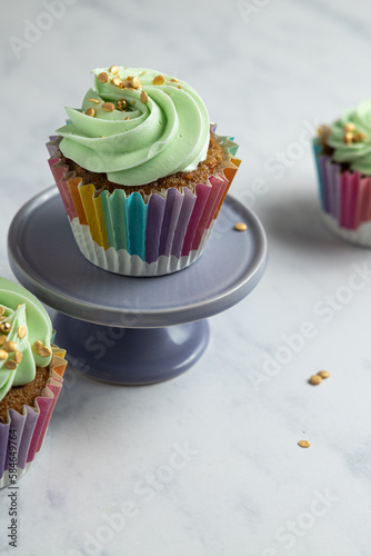 Three carrot cupcakes, with green frosting, one on a purple pedestal.