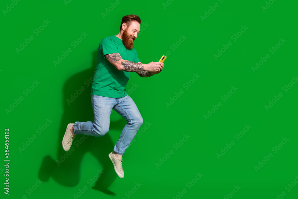 Full size photo of handsome man wear trendy t-shirt running hold smartphone amazing internet speed isolated on green color background Full size photo of handsome man wear trendy t-shirt running hold smartphone amazing internet speed isolated on green color background