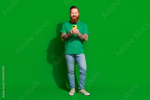 Full length photo of attractive positive man wear t-shirt chatting instagram twitter telegram facebook isolated green color background