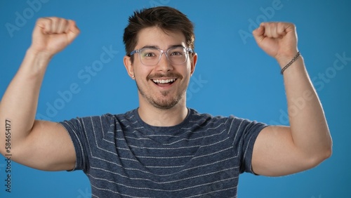 Shocked amazed say wow doing winner gesture put hands up young man 20s posing isolated on blue background studio. People lifestyle concept.