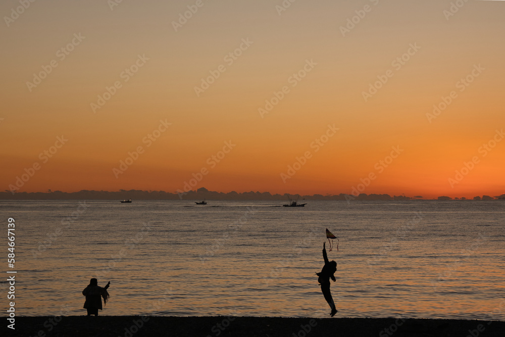 夕焼けの海岸で凧揚げ