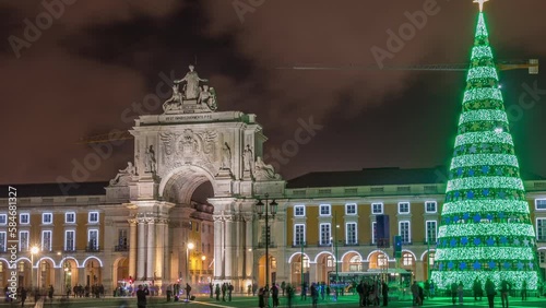 Commerce square illuminated and decorated at Christmas time in Lisbon night timelapse hyperlapse. Commercio square with christmas tree and people tourists crowd around, city of europe