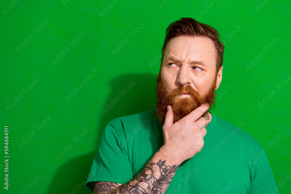 Photo of doubtful unsure guy dressed t-shirt looking empty space arm chin isolated green color background - obrazy, fototapety, plakaty 