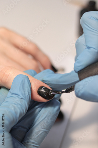 At the nail salon. Manicurist applies dark gel polish. The process of creating a manicure