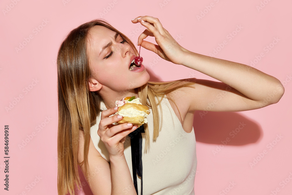 One beautiful model eating cake with pleasure facial expression over pink background One beautiful model eating cake with pleasure facial expression over pink background