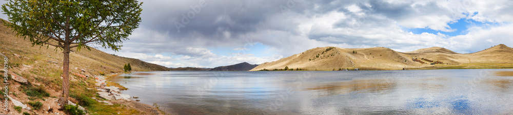 Panoramic view of Baikal Lake in August day. Scenic summer landscape of Tutay Bay coastline with blue water and green larch tree on the beach. Summer travel and outdoors