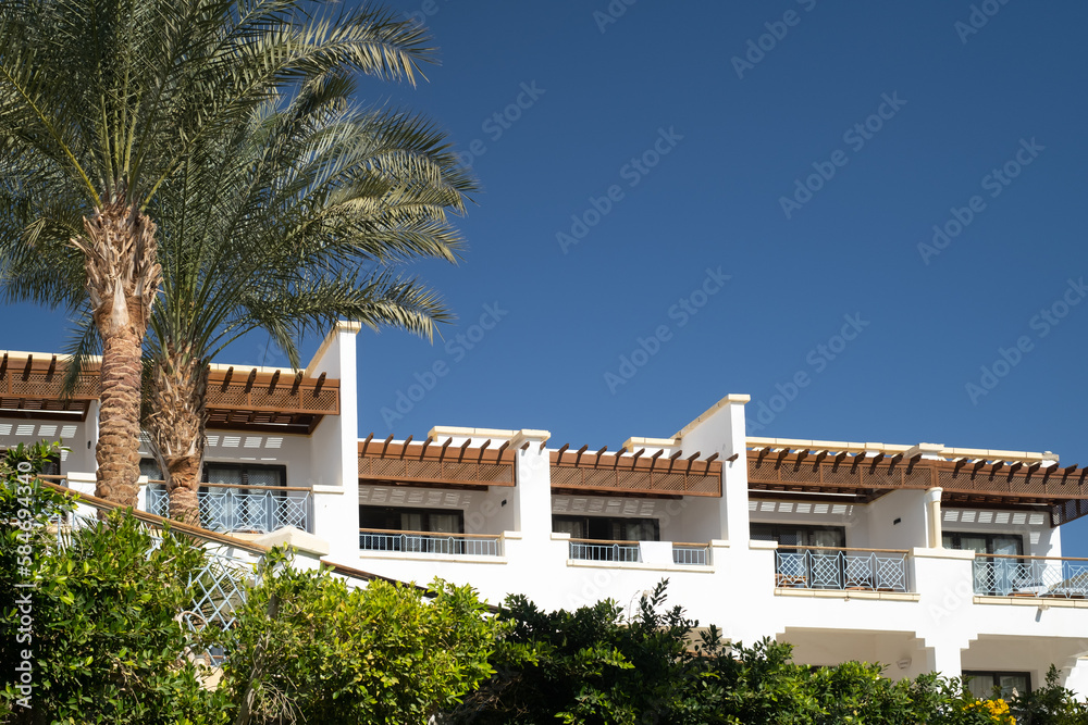 Fototapeta premium Palm trees against white home by the beach with blue sky and sand The top of the house or apartment with nice window